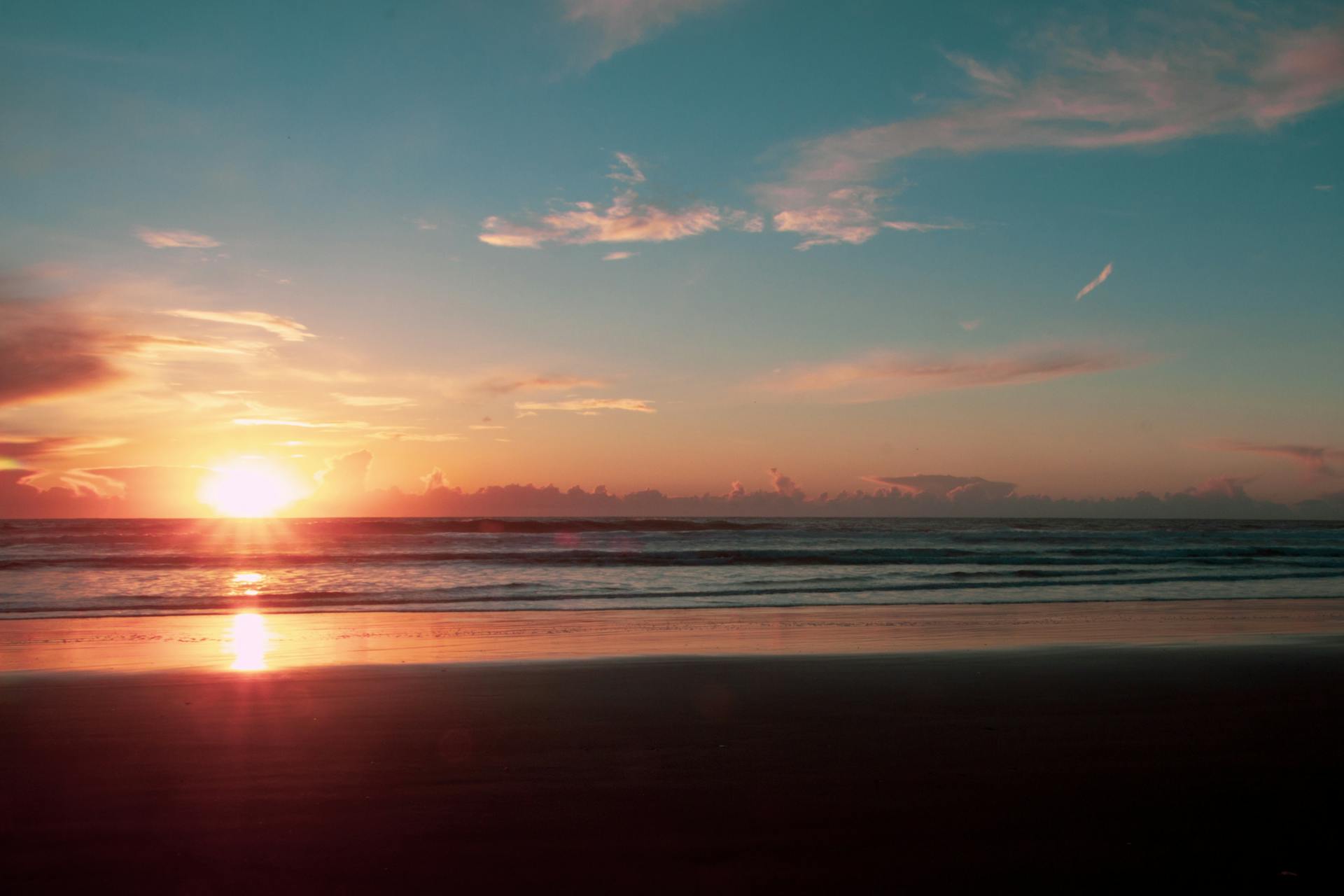 A tranquil beach sunset with vivid colors reflecting on the sand and sea, capturing a peaceful seascape.