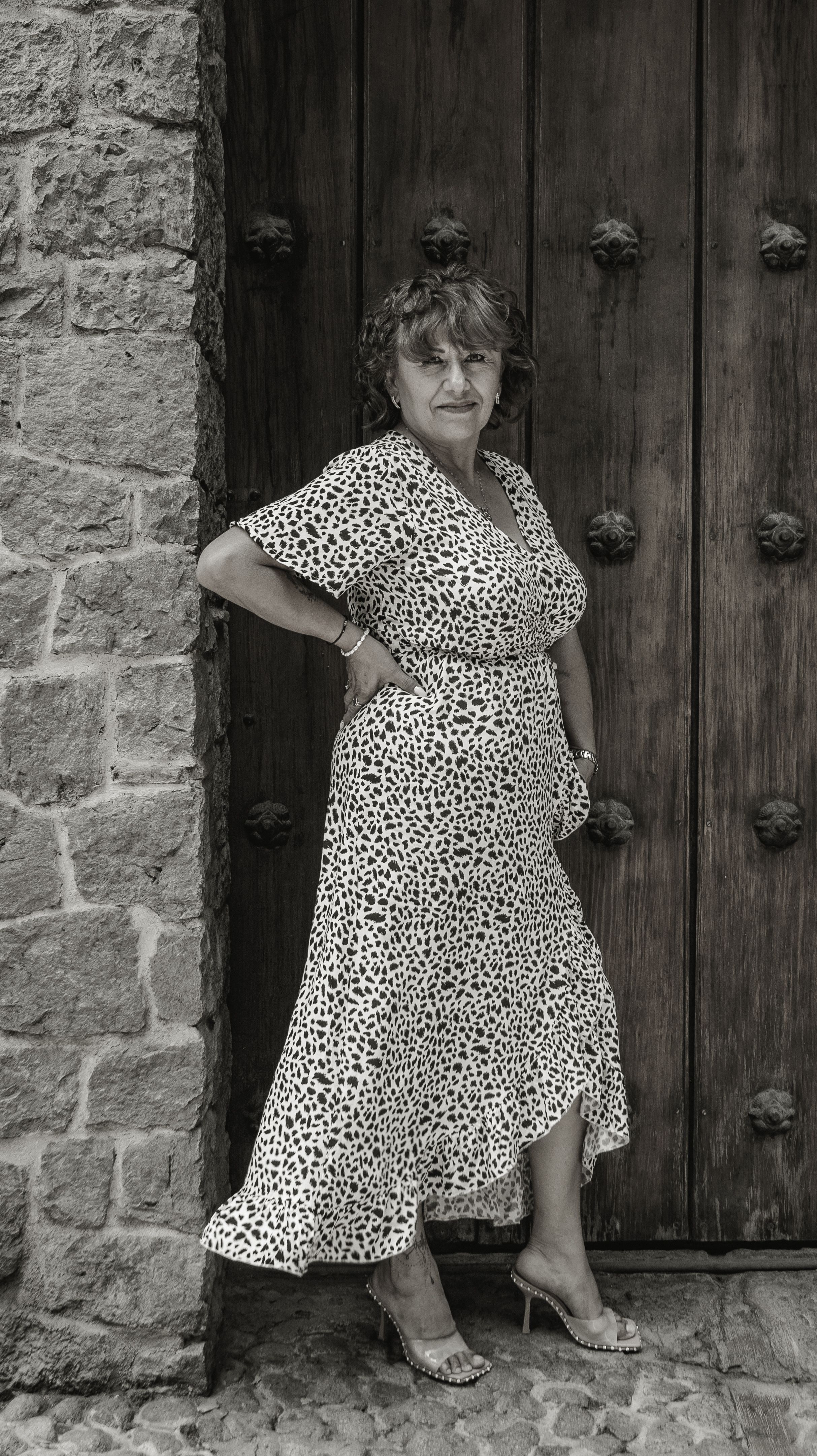 Elegant woman posing by a rustic doorway in Puebla, Mexico, showcasing sophisticated fashion.