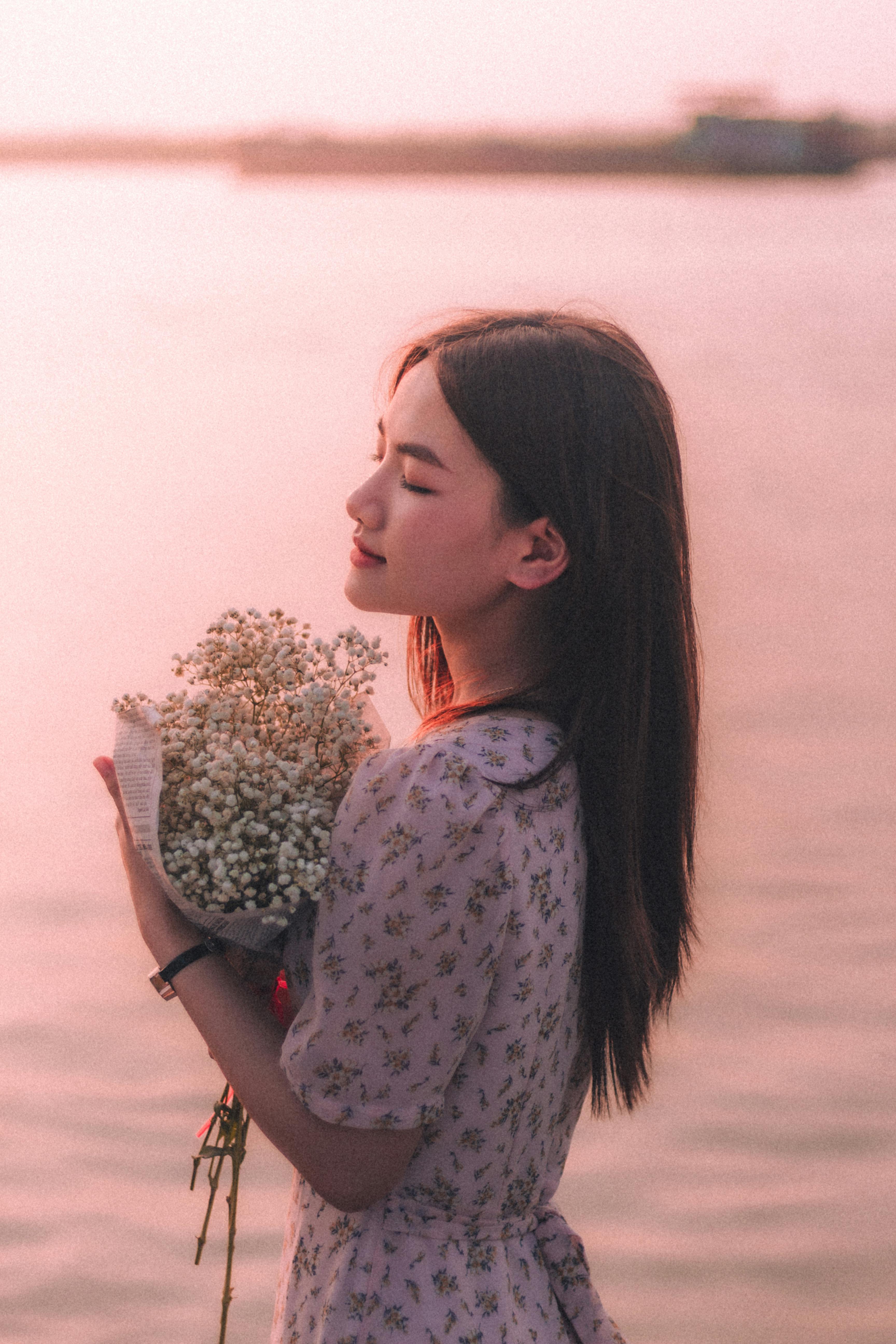 Young woman holding bouquet, embracing serenity by the water at sunset.