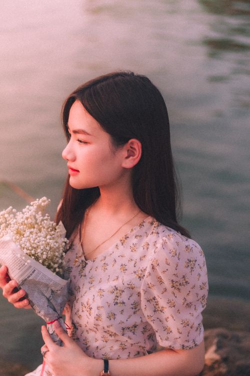 Free A serene young woman holds a bouquet by calm water at sunset, embracing nature's beauty. Stock Photo