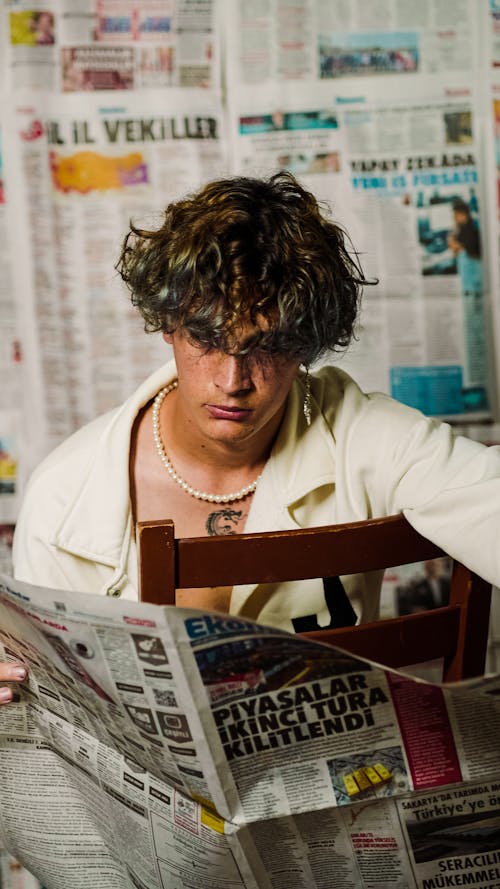 Young Man Sitting in a Room with Newspapers on the Wall and Holding a Newspaper