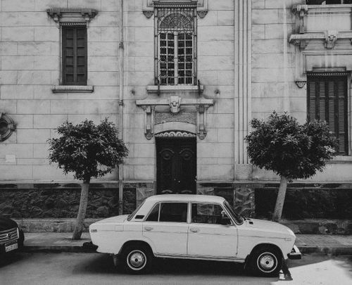 Free Classic vintage car parked on an urban street beside a historic building facade in black and white. Stock Photo