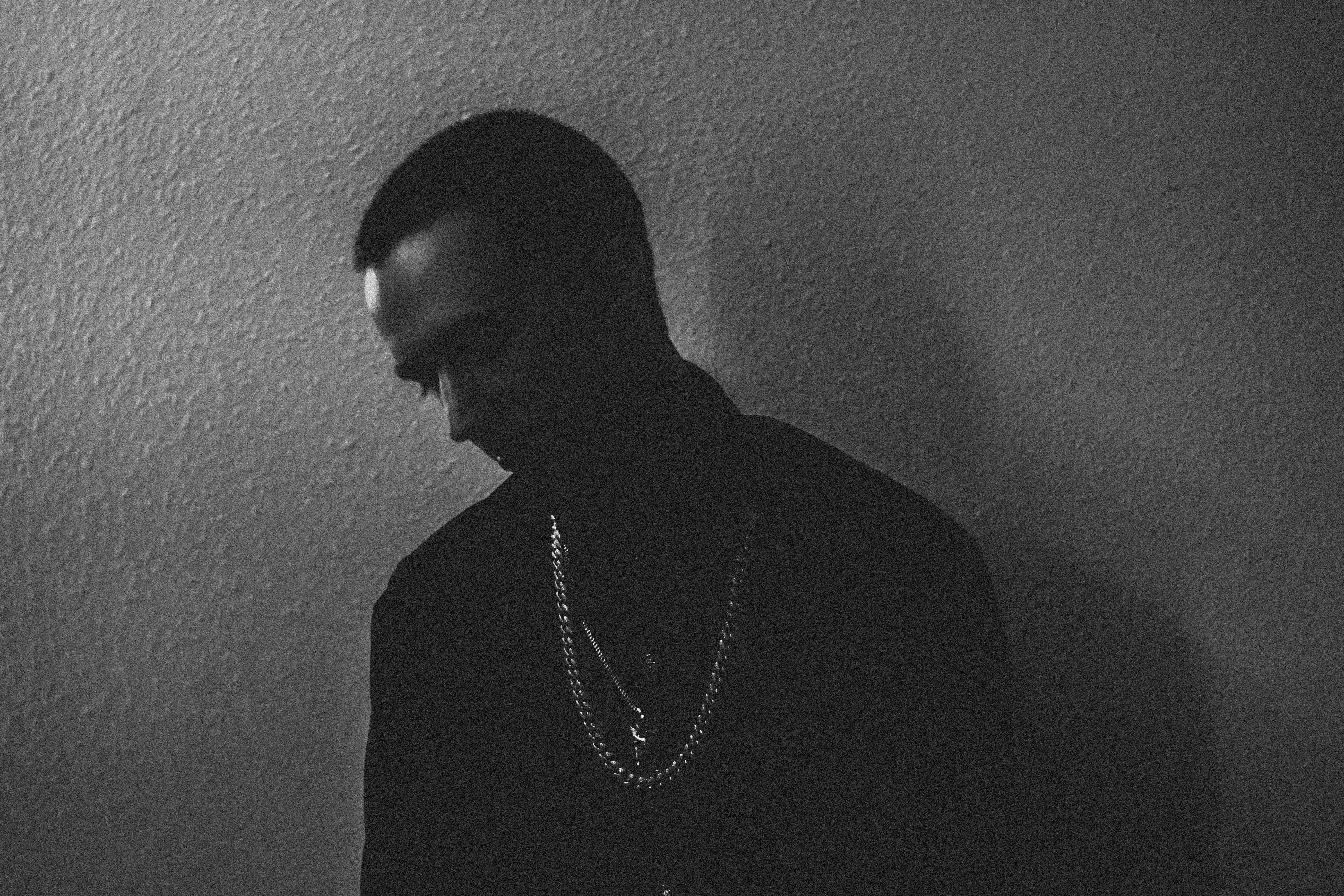 一幅描绘着喜怒无常的黑白肖像中，一个男人戴着链子靠在纹理墙壁上