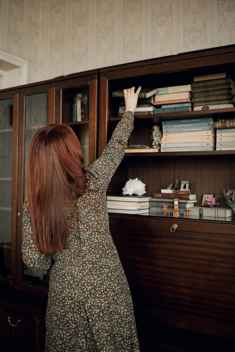 Back View Of A Young Woman Reaching For A Book On The Top Shelf 