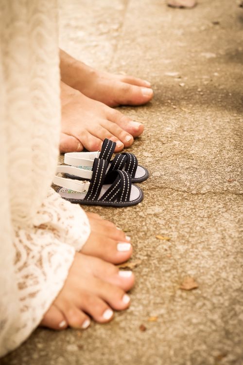 Free Close-up of a pregnant woman's bare feet next to sandals on a sunlit pavement. Stock Photo