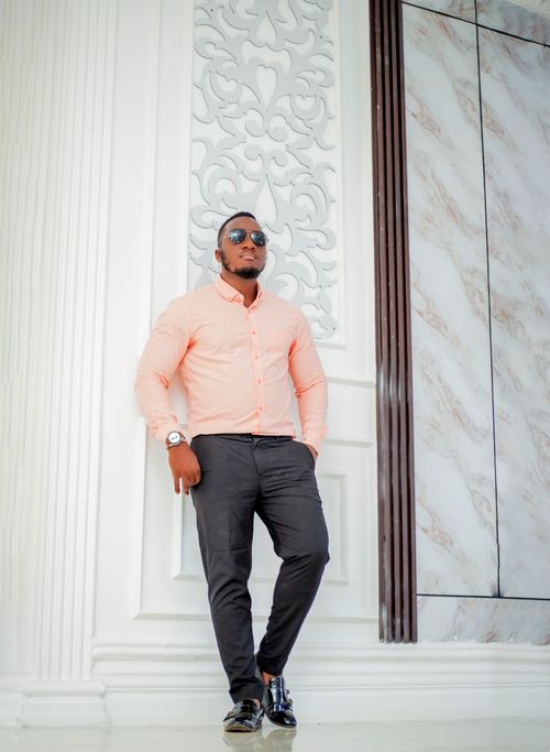 Free Fashionable young man leaning against elegant white interior with ornate design, wearing sunglasses. Stock Photo