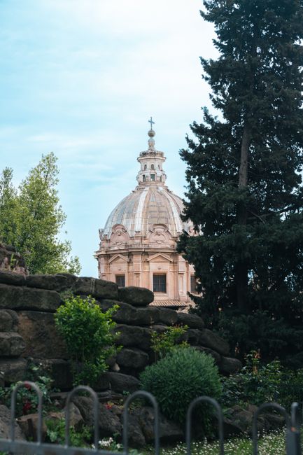 Elegant dome architecture peeking through lush greenery in Rome, Italy.