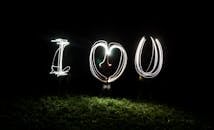 一幅采用深色艺术风格的长曝光灯光画，呈现“我爱你”字样，非常适合作为浪漫或情人节的背景