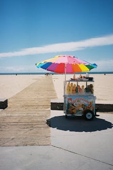 Vibrant fruit stand with umbrella on sandy beach, perfect for summer relaxation.