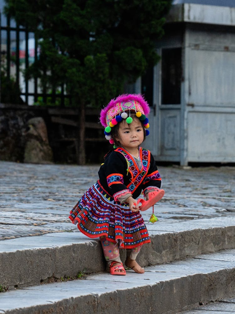 Cute Little Girl In Traditional Clothing Standing And Holding Her Shoe 