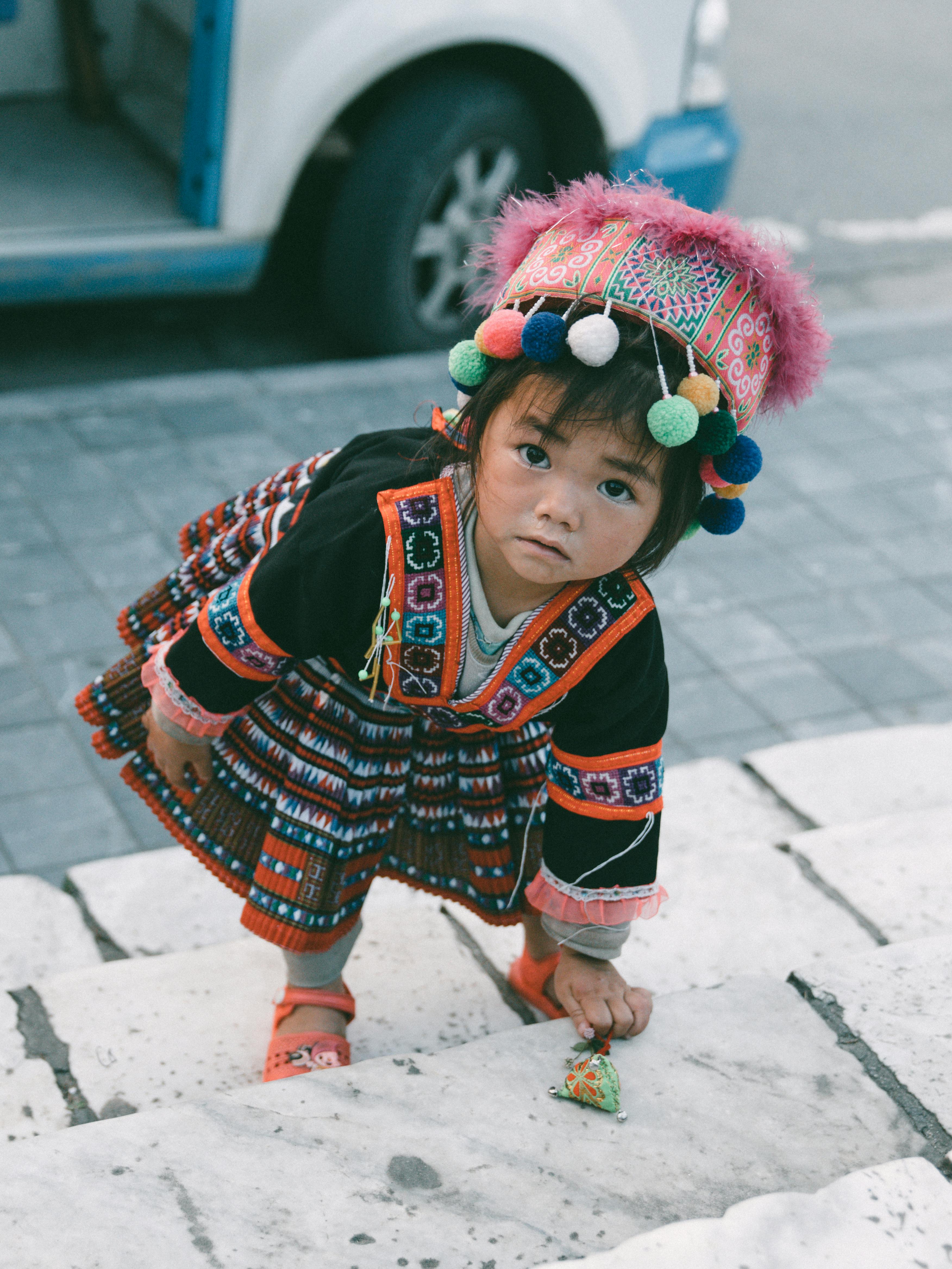 A young child in colorful traditional clothing climbing steps outdoors.