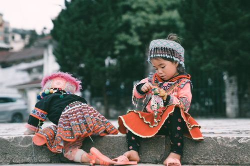Free Two children in vibrant traditional clothing sitting outdoors on a stone ledge. Stock Photo