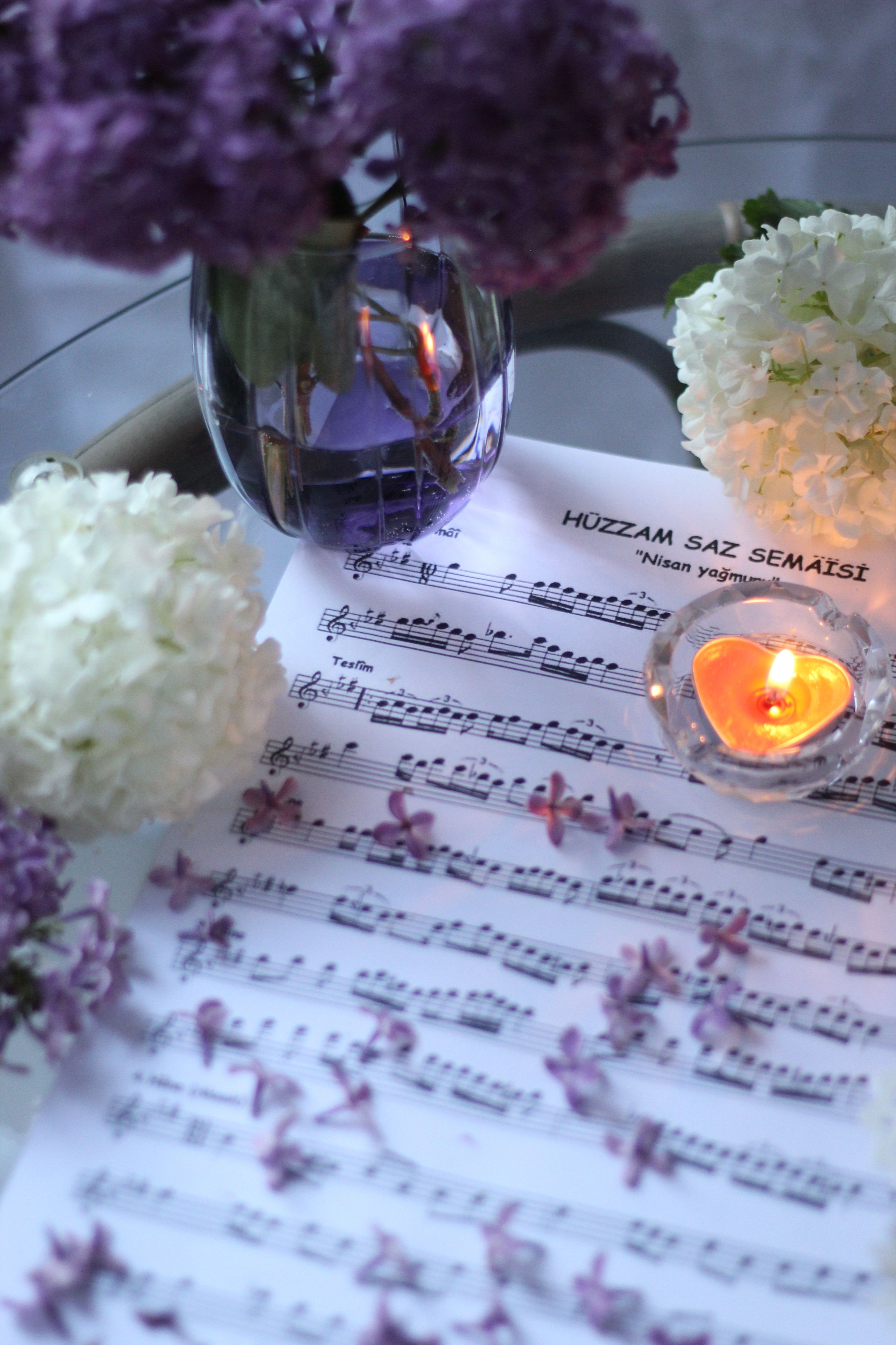 A tranquil scene with flowers, a heart-shaped candle, and sheet music on a table.