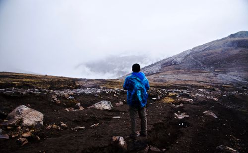 Free A hiker in a blue jacket stands alone on a foggy mountain landscape, embodying adventure and solitude. Stock Photo