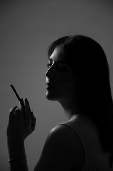 Elegant black and white portrait of a woman holding a cigarette in a shadowy atmosphere.