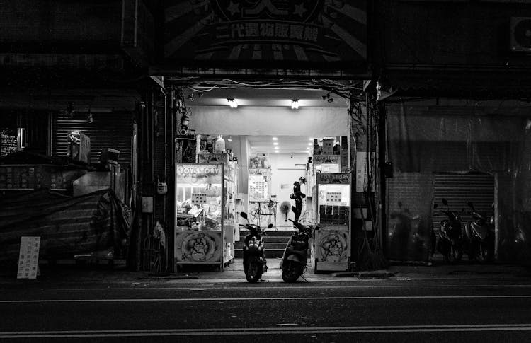 Motorbikes Parked At The Entrance To A Shop At Night