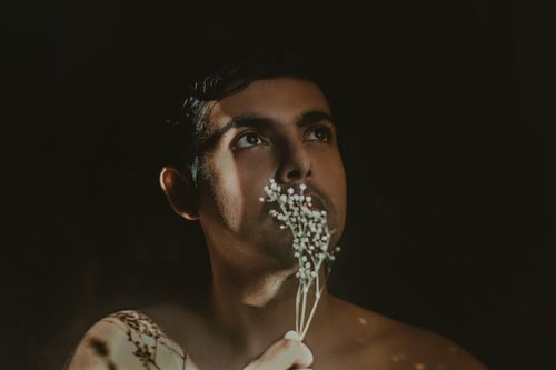 Free A man holding delicate flowers in a moody light setting, exuding introspection and thoughtfulness. Stock Photo