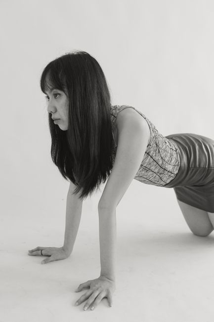 Black and white studio photo of a young woman in contemporary fashion posing on hands and knees.