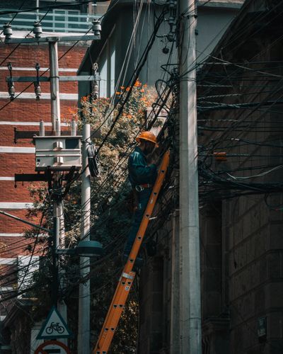 Man in Helmet Working on Ladder near Poles and Wires · Free Stock Photo