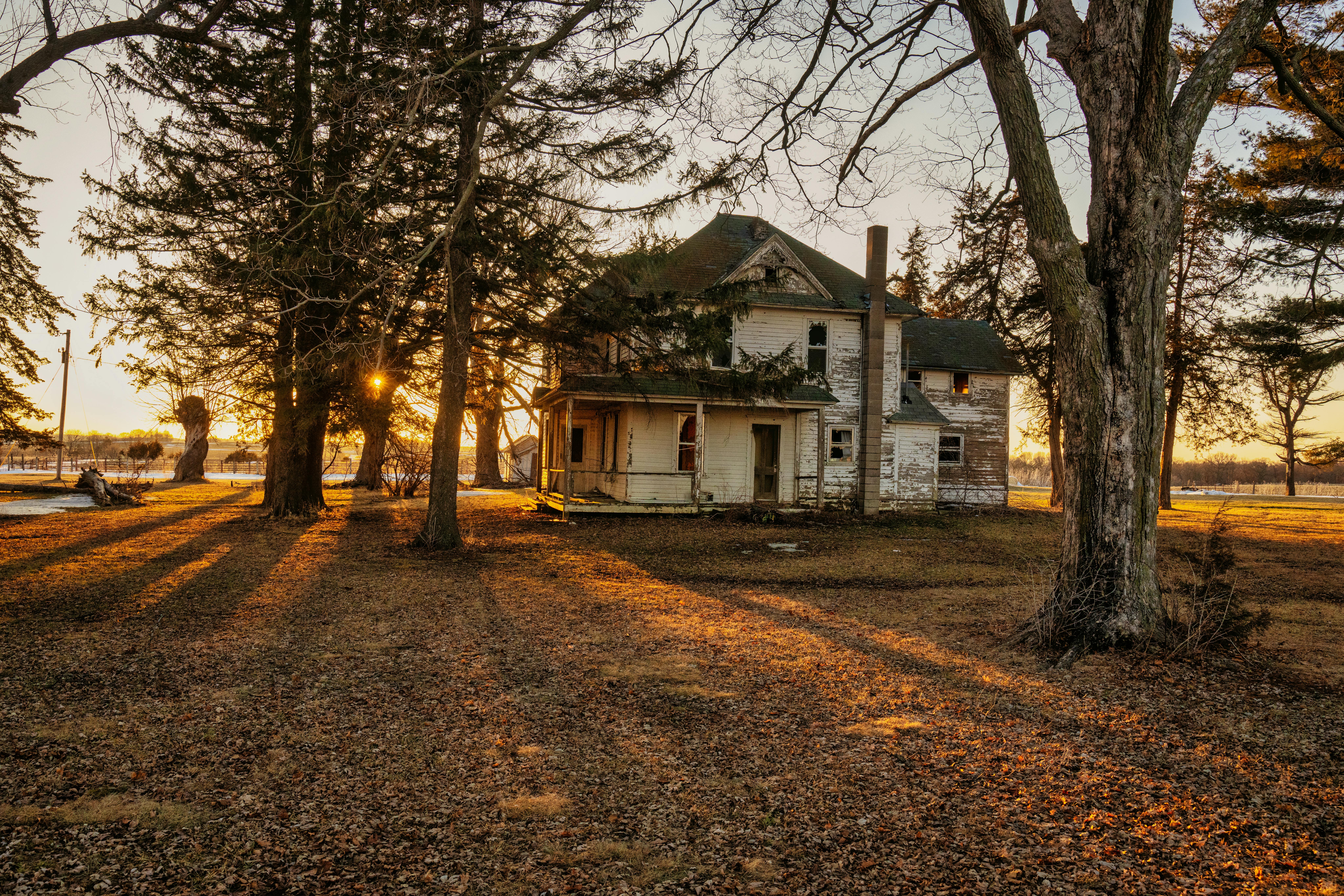 Rustic, abandoned farmhouse in Minnesota's countryside, beautifully lit by a warm sunset.