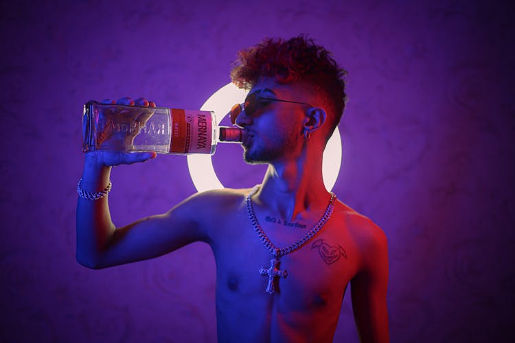 Studio Shot Of A Young Shirtless Man Drinking Alcohol From A Bottle 