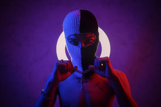 A topless, masked individual holding a chain against a luminous backdrop in a studio setting.