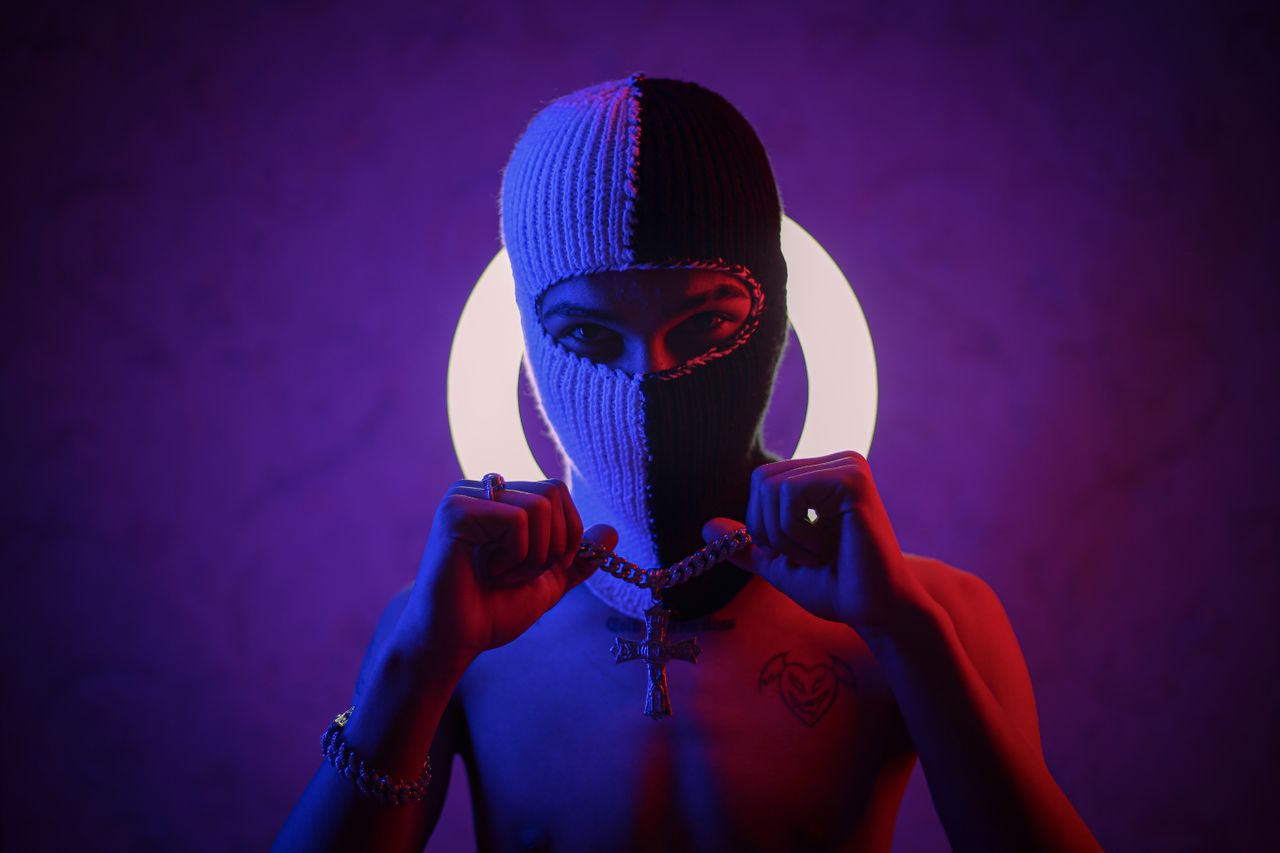 a topless masked individual holding a chain against a luminous backdro