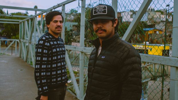 Two men standing on a pedestrian overpass in Tijuana, Mexico, during the day.