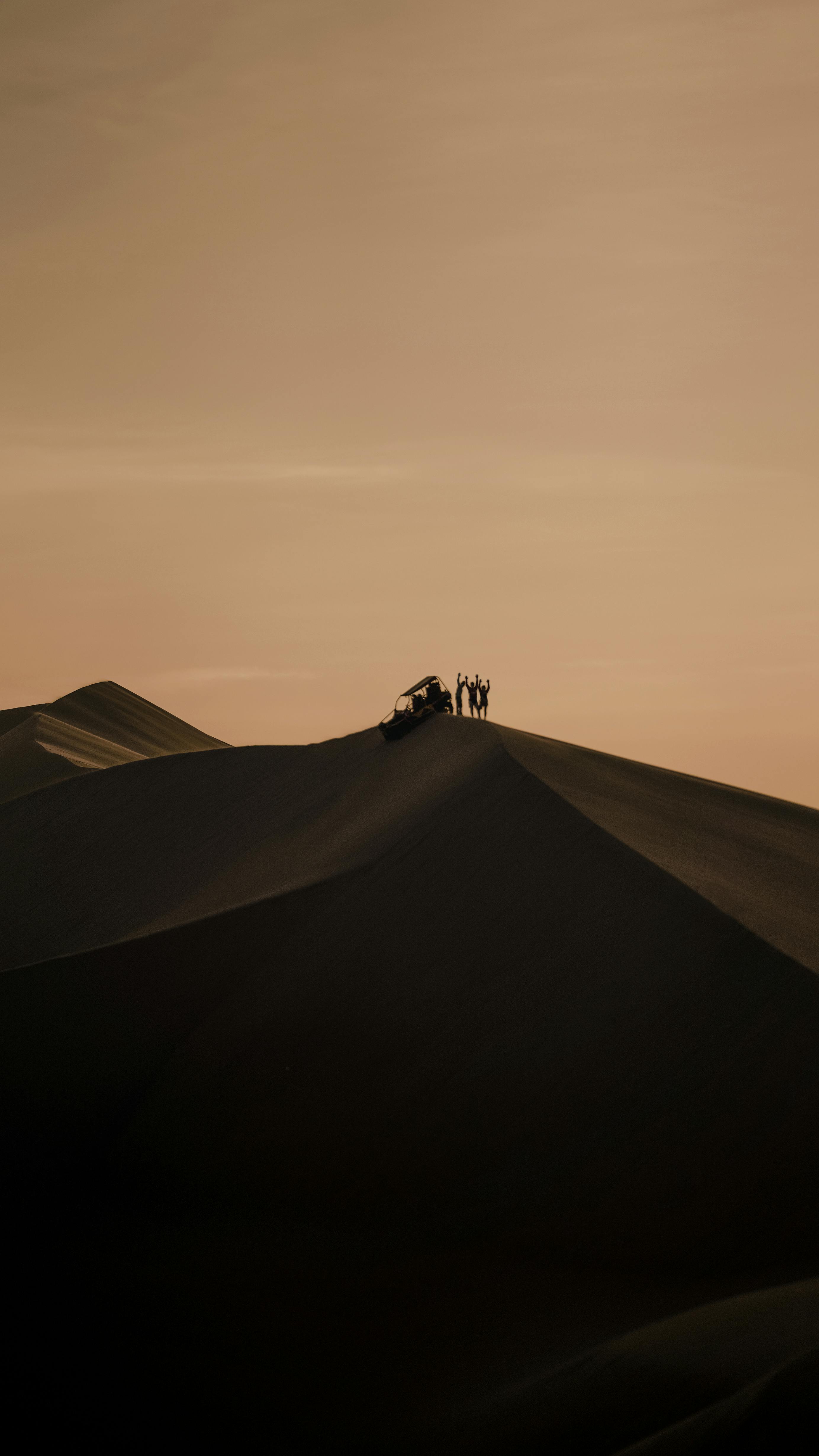 Silhouetted figures atop sand dunes in Ica, Peru, captured during sunset. A scene of adventure and tranquility.