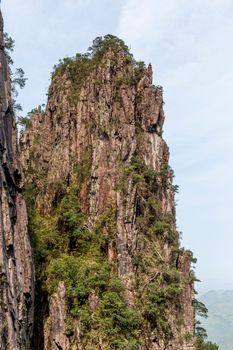 Impressive rocky cliff face surrounded by lush green vegetation under clear skies.