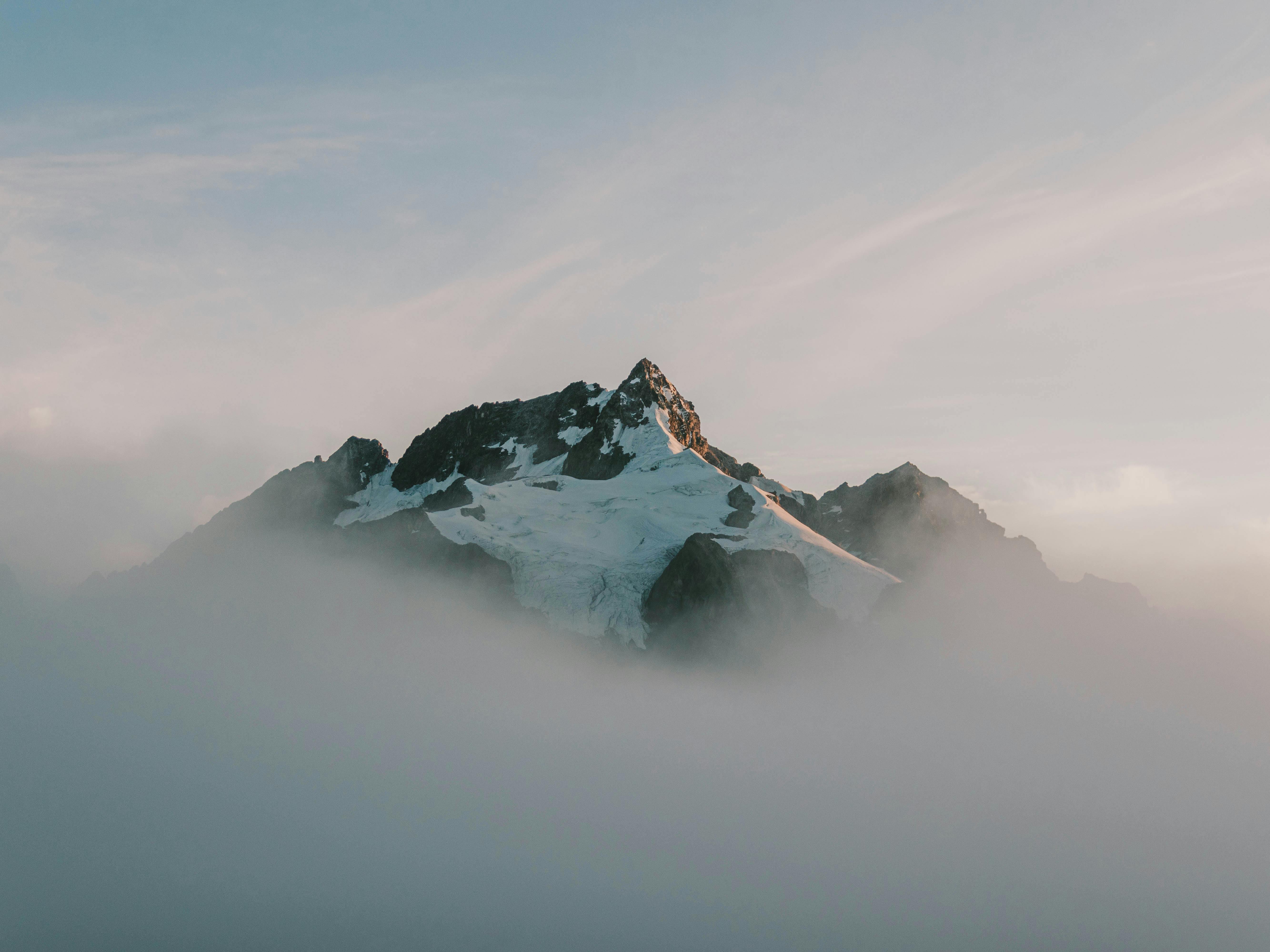 A majestic snow-capped mountain peak emerging above the clouds in a tranquil setting.
