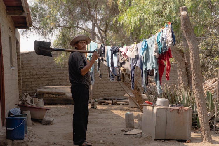 Man With Shovel Standing Near Drying Clothes