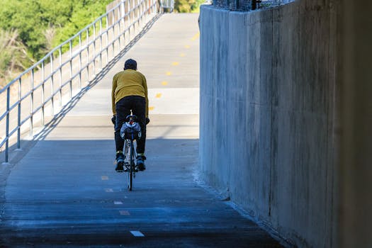 A man cycling under an urban bridge, enjoying a sunny day on a dedicated bike path.