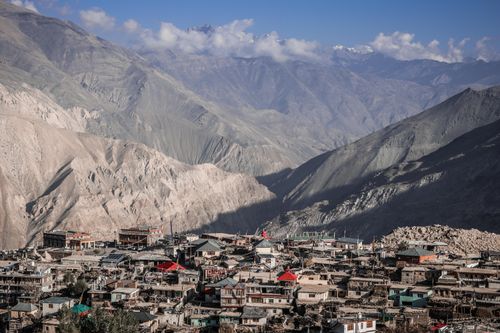 Free Scenic view of a sunlit village nestled in a mountainous valley under a clear blue sky. Stock Photo