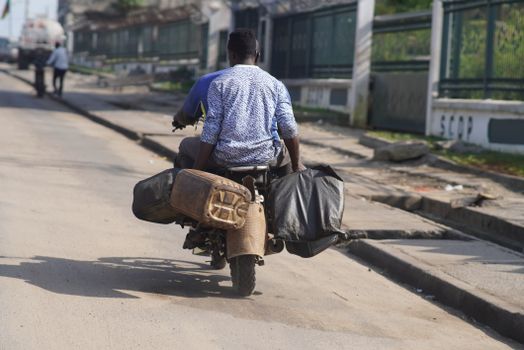 A man rides a motorbike with luggage on a sunny day in Douala, Cameroon.