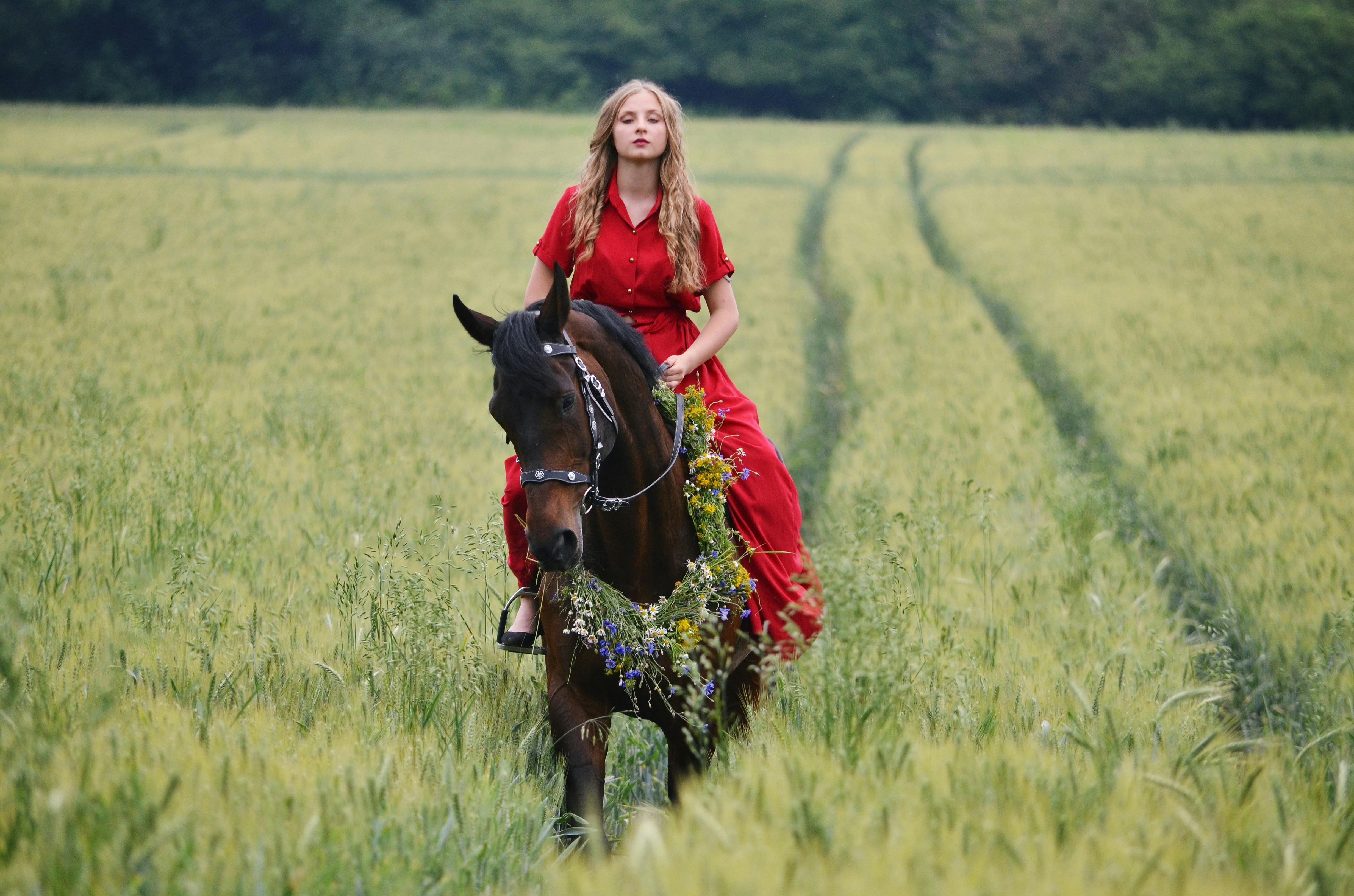 young woman in a red dress riding a horse through the field