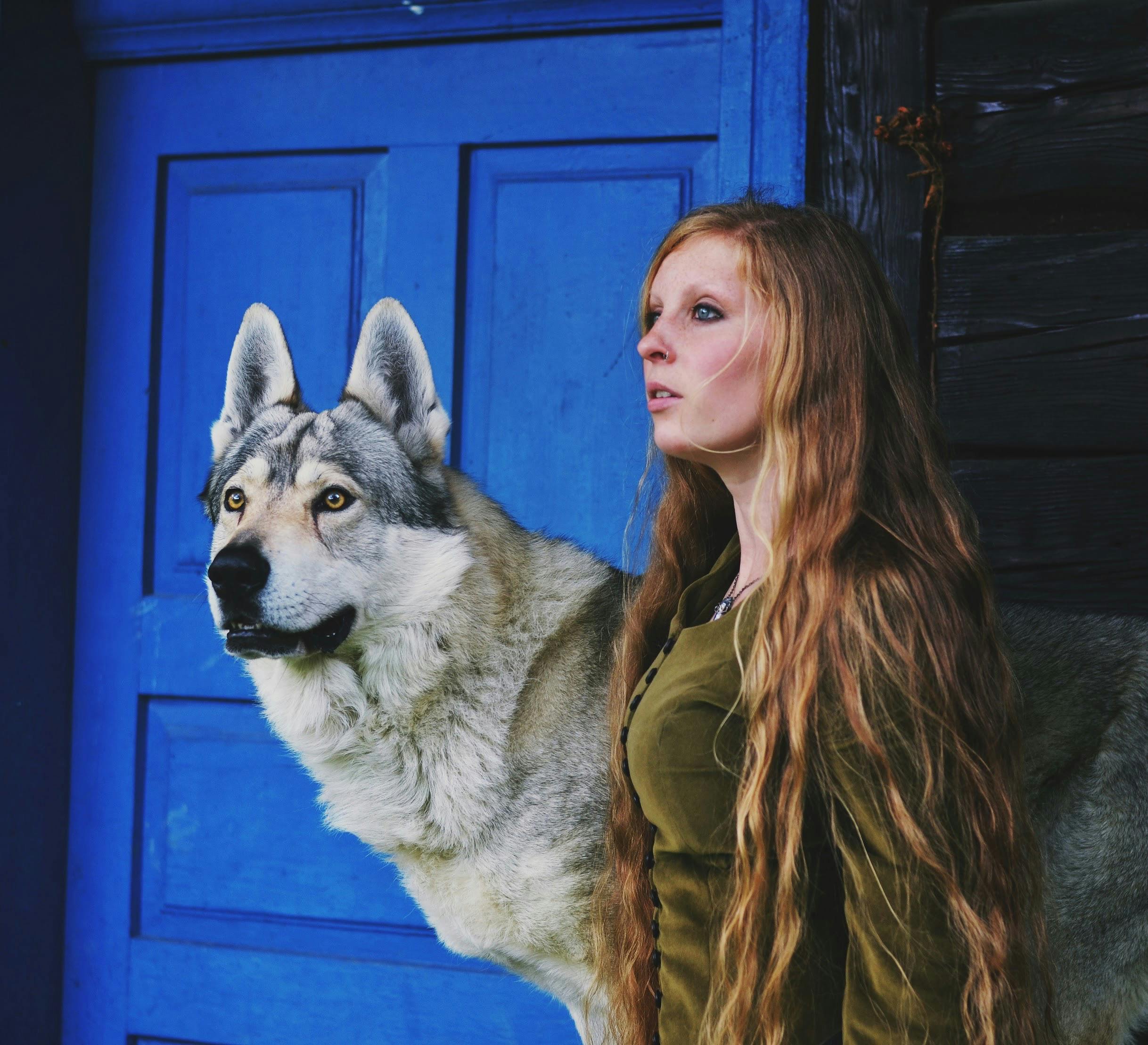 Woman with long blonde hair stands with a wolf-dog against a striking blue door background.