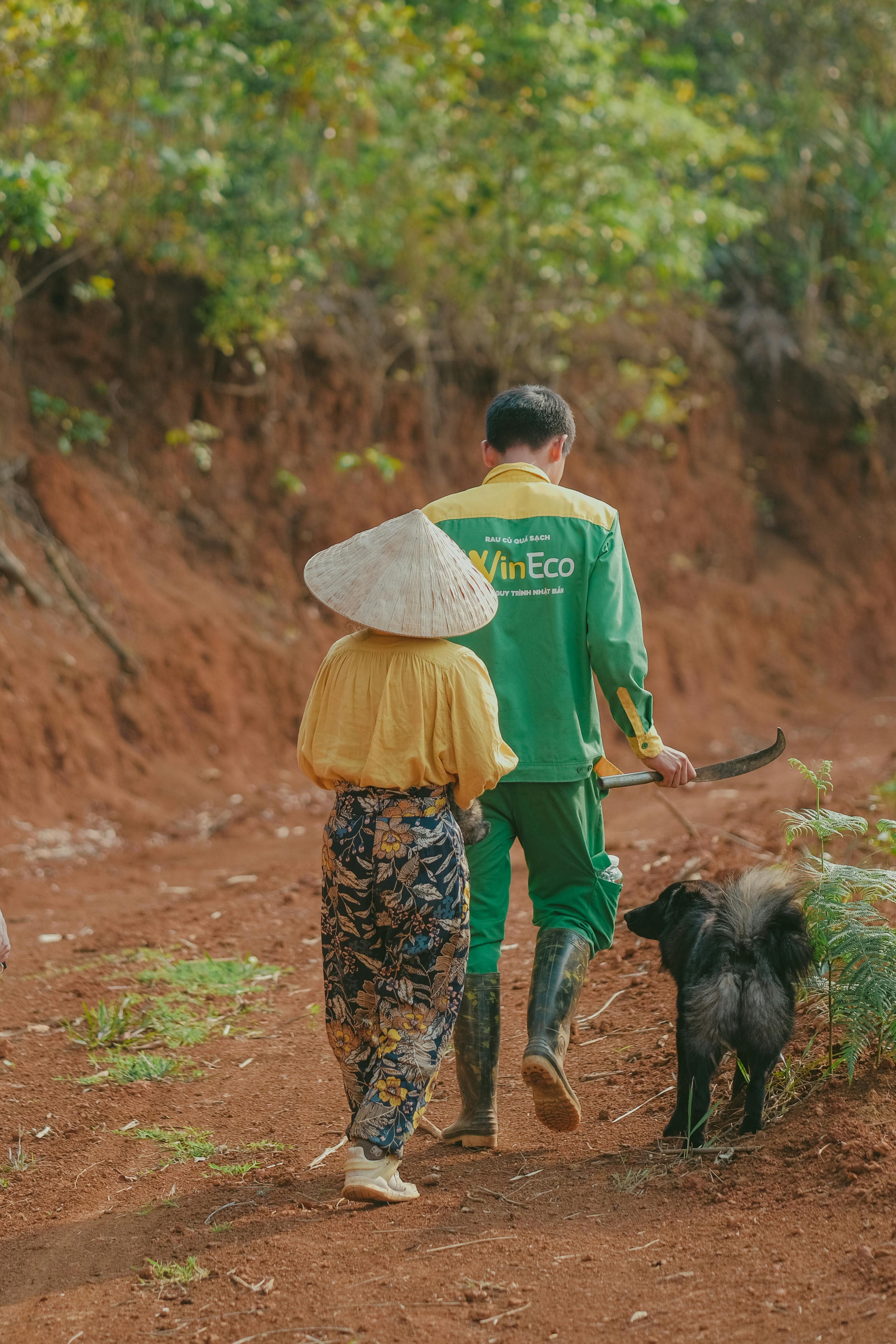 Man and woman walking a dog on a rural dirt path, wearing traditional attire.