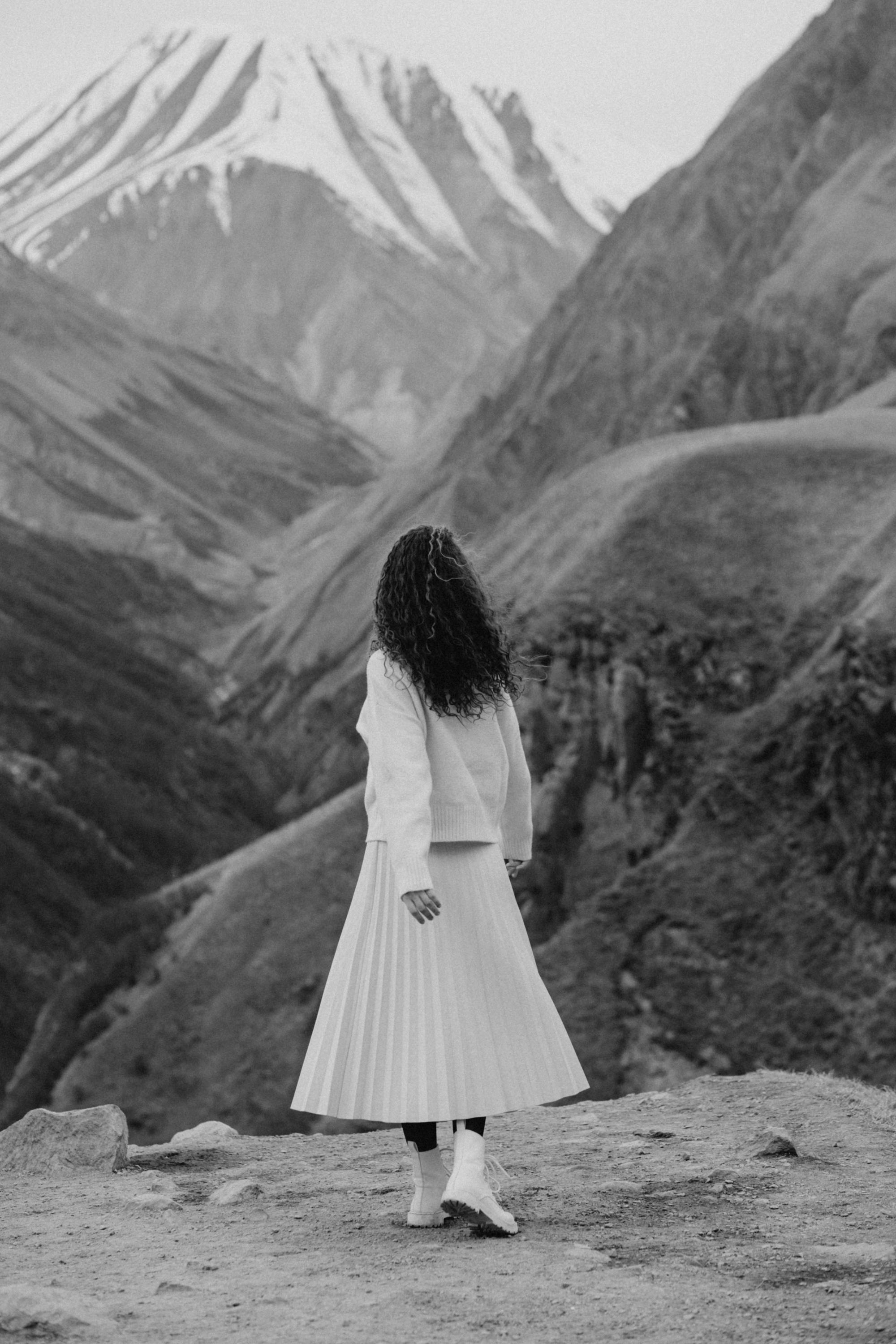 Woman in skirt and sweater exploring mountainous landscape in black and white.