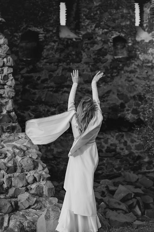 Woman in Long Dress Standing with Arms Raised in Ruins