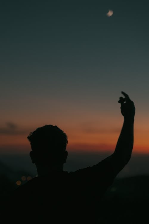 Silhouette of a Man Rising a Hand against the Sky at Dusk