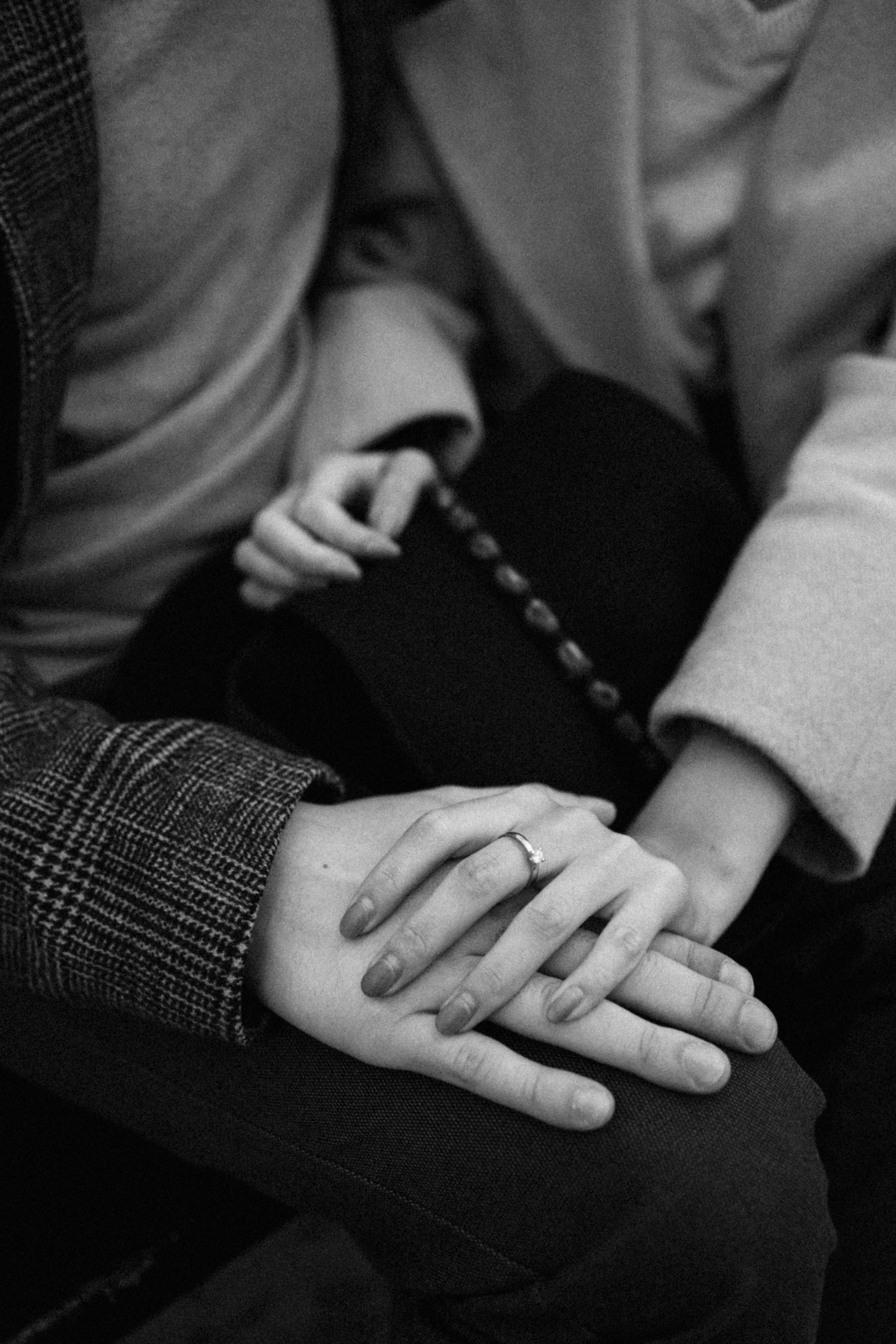 Black and white photo of a couple holding hands, showcasing an engagement ring.
