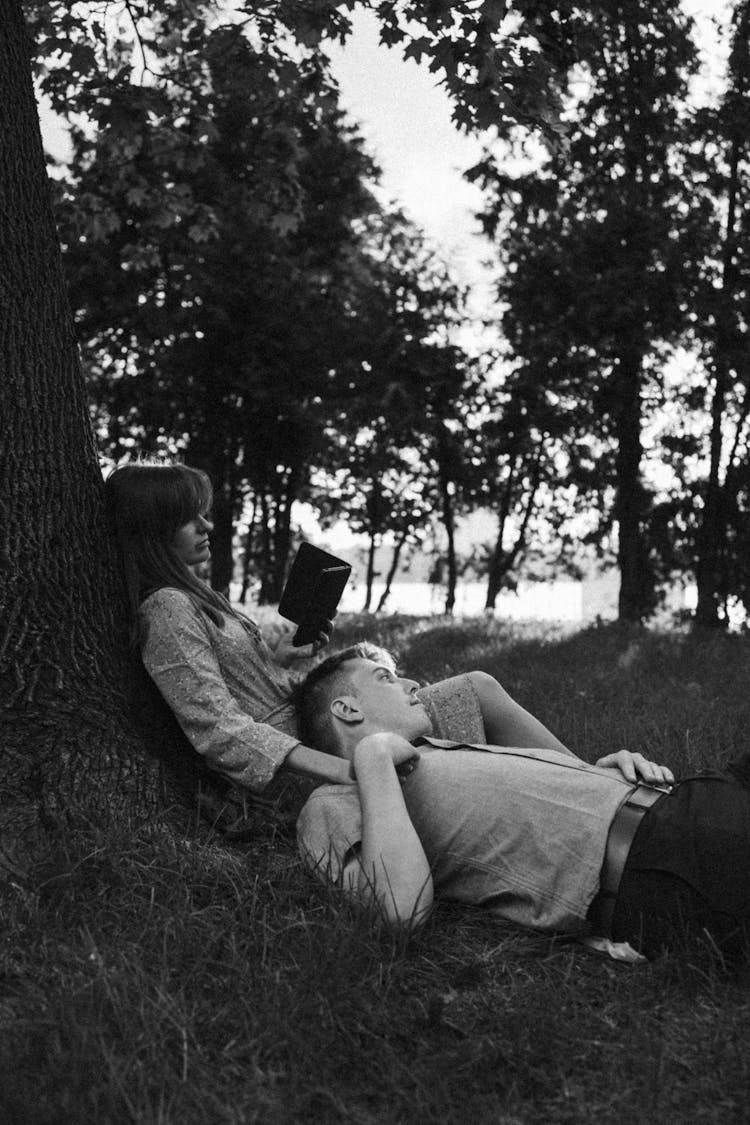 A Couple Laying On The Grass In A Park 