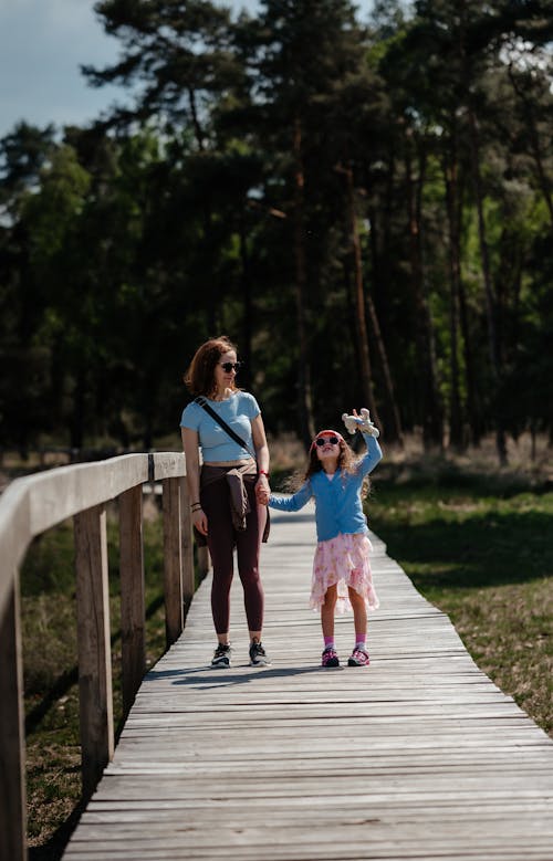 Mother with Daughter on Wooden Footpath in Forest