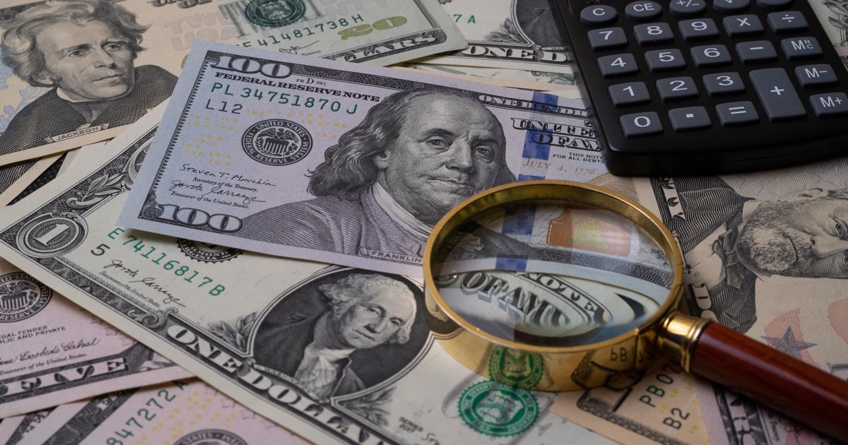 US currency bills with magnifying glass and calculator, symbolizing financial analysis.