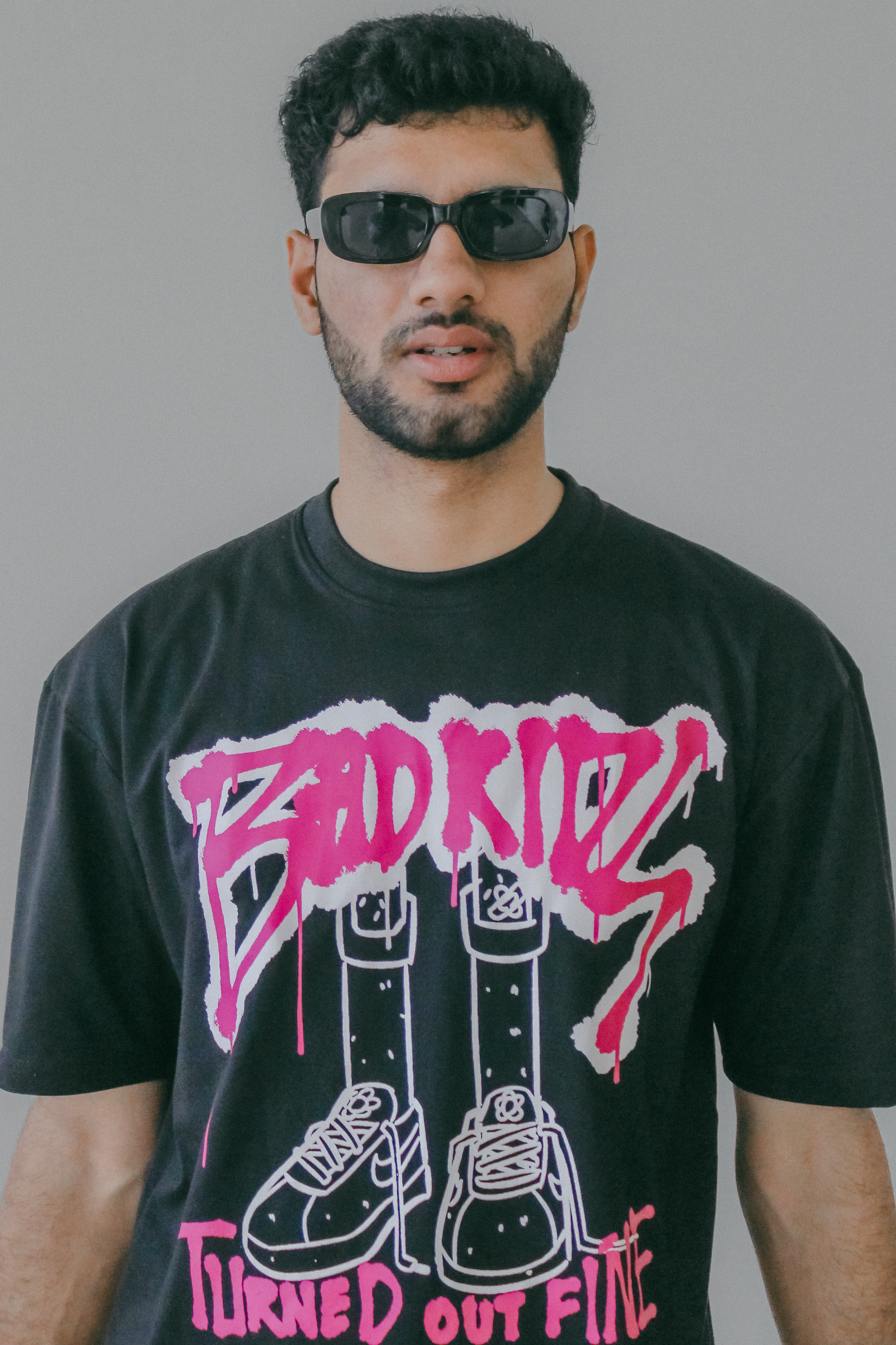 Stylish young man in sunglasses wearing graphic tee, striking a cool pose.