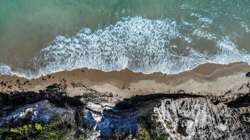 Free Relaxing aerial view of waves washing over a tranquil sandy beach with rocky coastline. Stock Photo