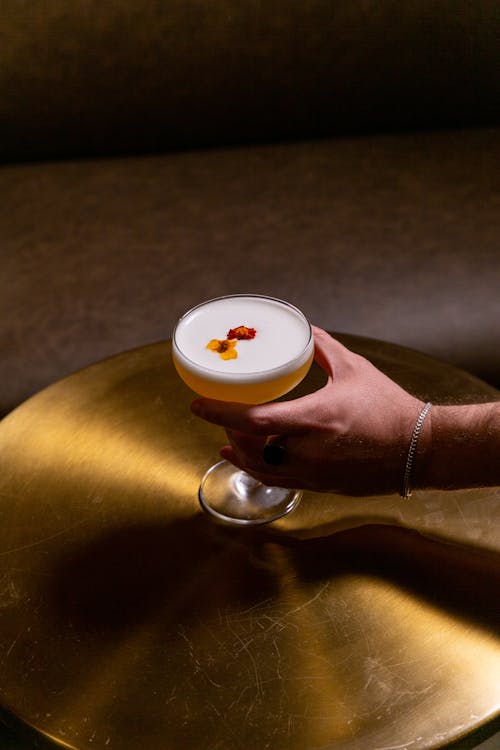 A Person Taking a Glass of Martini Cocktail from a Round Shiny Metal Table 