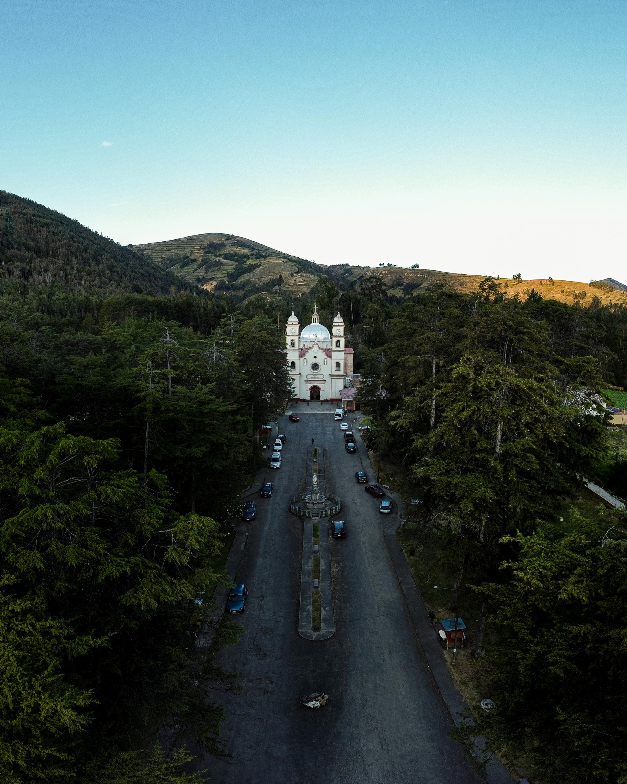 A stunning aerial photo capturing a church surrounded by lush hills and forests.