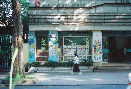 Free A woman wearing casual clothing walks past an urban bookstore on a sunny day. Stock Photo